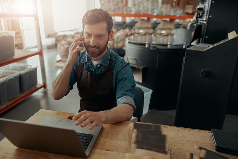 Business owner multitasking with phone and laptop, showcasing integrated rural business solutions.