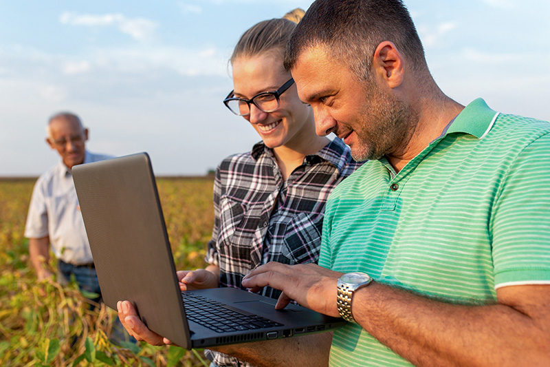 Farmers using a laptop in a field, showcasing broadband access in agricultural areas.
